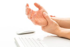 A person sitting at a computer struggling with wrist pain from carpal tunnel.