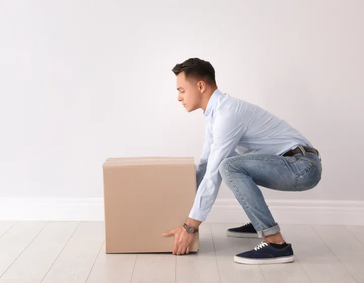 A man squatting down to pick up a box