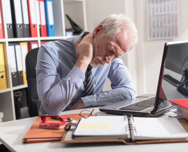 A man sitting a desk and holding his neck in pain